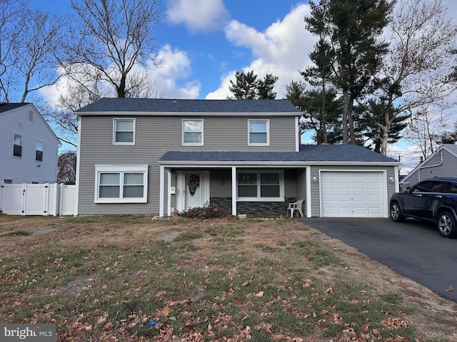 traditional home with a garage, driveway, stone siding, fence, and a front yard