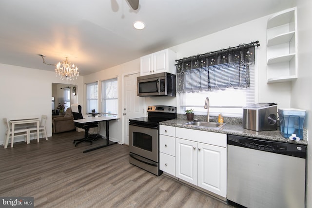 kitchen with a notable chandelier, appliances with stainless steel finishes, white cabinets, a sink, and wood finished floors