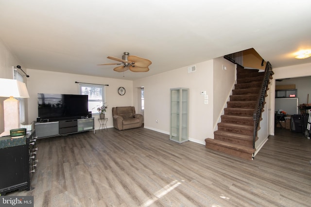 living room with visible vents, baseboards, ceiling fan, stairway, and wood finished floors