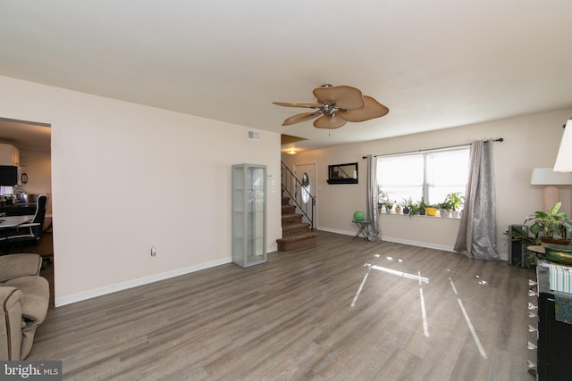 living area featuring wood finished floors, a ceiling fan, visible vents, stairs, and baseboards