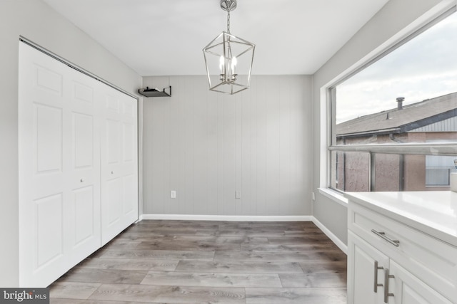 unfurnished dining area with wood walls, plenty of natural light, hardwood / wood-style floors, and a notable chandelier