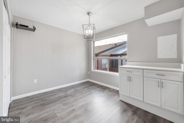 unfurnished dining area with a notable chandelier, wood-type flooring, and wooden walls