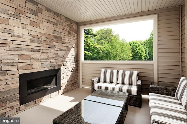 sunroom / solarium with plenty of natural light, an outdoor stone fireplace, and wood ceiling