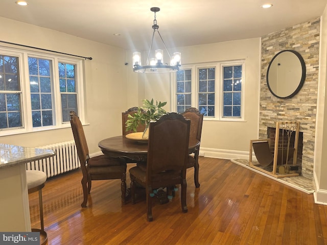 dining space featuring a notable chandelier, dark hardwood / wood-style floors, a stone fireplace, and radiator