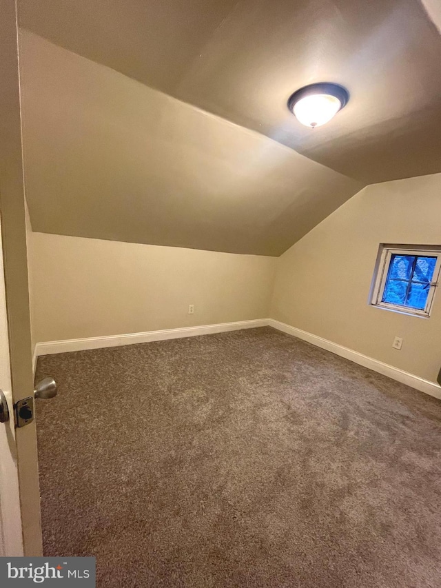 bonus room with dark carpet and vaulted ceiling