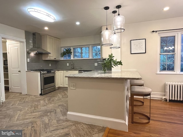 kitchen with wall chimney exhaust hood, stainless steel gas range oven, radiator heating unit, and backsplash