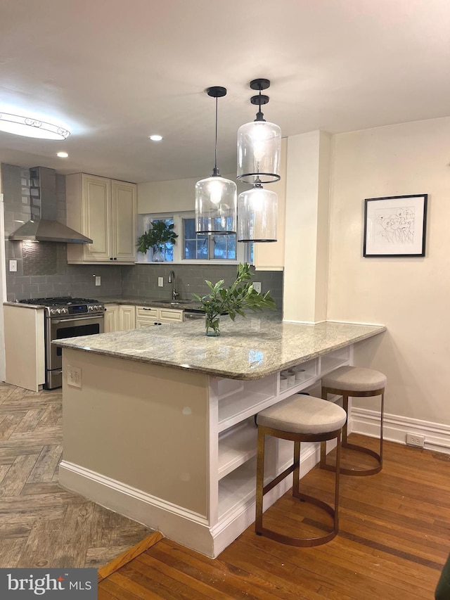 kitchen with stainless steel range with gas cooktop, wall chimney range hood, tasteful backsplash, kitchen peninsula, and a breakfast bar area