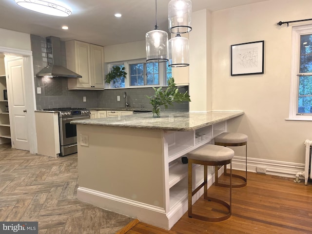 kitchen with stainless steel gas stove, wall chimney exhaust hood, kitchen peninsula, decorative light fixtures, and decorative backsplash