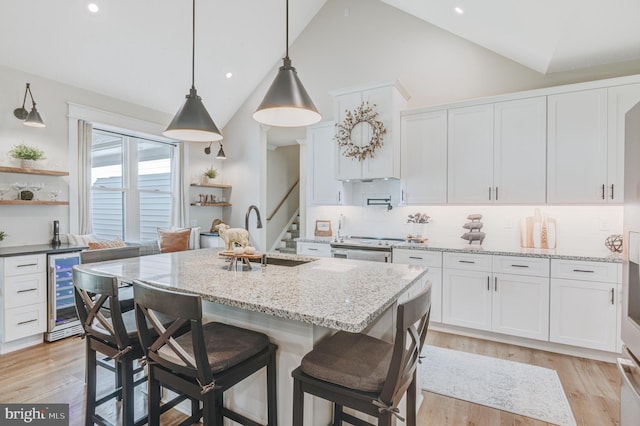 kitchen featuring light stone countertops, backsplash, a kitchen island with sink, light hardwood / wood-style flooring, and white cabinets