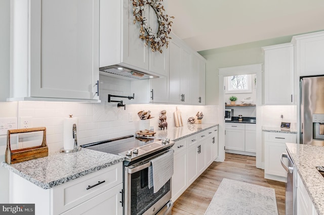 kitchen with decorative backsplash, light stone counters, stainless steel appliances, white cabinets, and light hardwood / wood-style floors