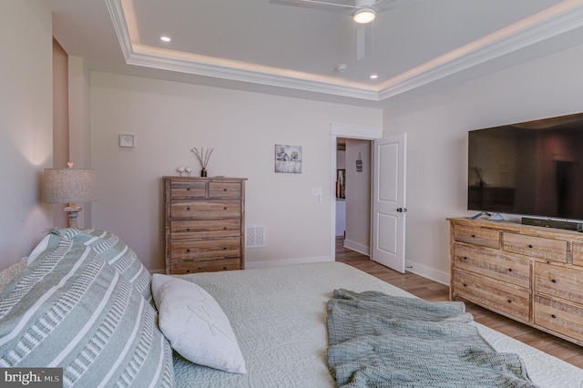 bedroom with ceiling fan, crown molding, a tray ceiling, and light hardwood / wood-style flooring