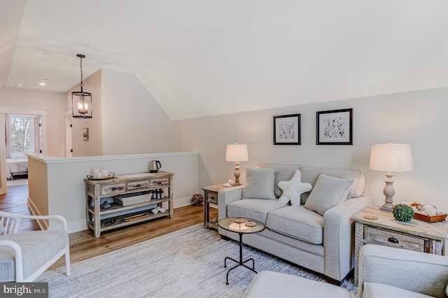 living room with a chandelier, light wood-type flooring, and lofted ceiling