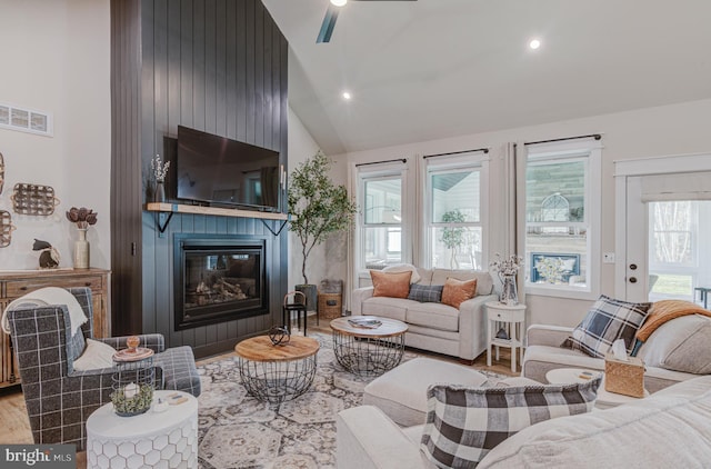 living room with a fireplace, high vaulted ceiling, a healthy amount of sunlight, and light wood-type flooring