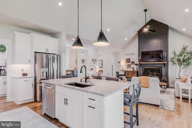 kitchen with white cabinetry, dishwasher, sink, a kitchen island with sink, and a fireplace