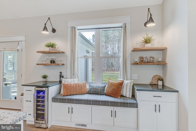 living area featuring bar area, light wood-type flooring, wine cooler, and plenty of natural light