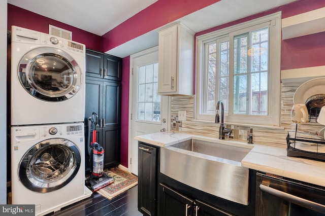 laundry area featuring dark hardwood / wood-style flooring, stacked washer / dryer, a healthy amount of sunlight, and sink