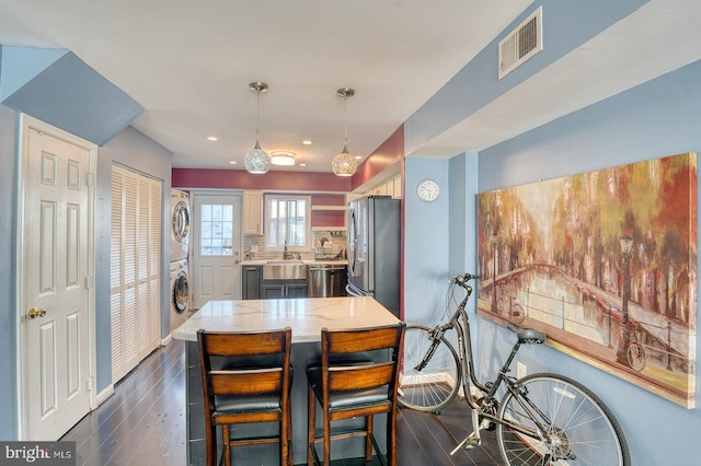 dining space with dark wood-type flooring, stacked washing maching and dryer, and sink