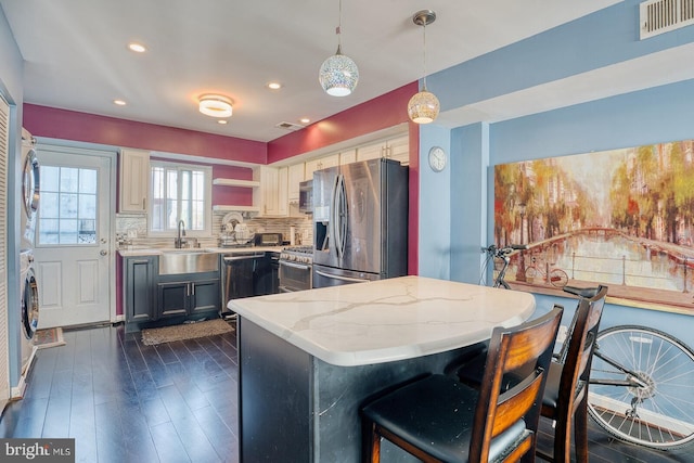 kitchen featuring light stone countertops, appliances with stainless steel finishes, decorative backsplash, stacked washing maching and dryer, and pendant lighting