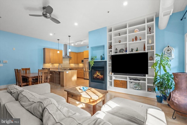 living room featuring light wood-type flooring, built in features, ceiling fan, and sink