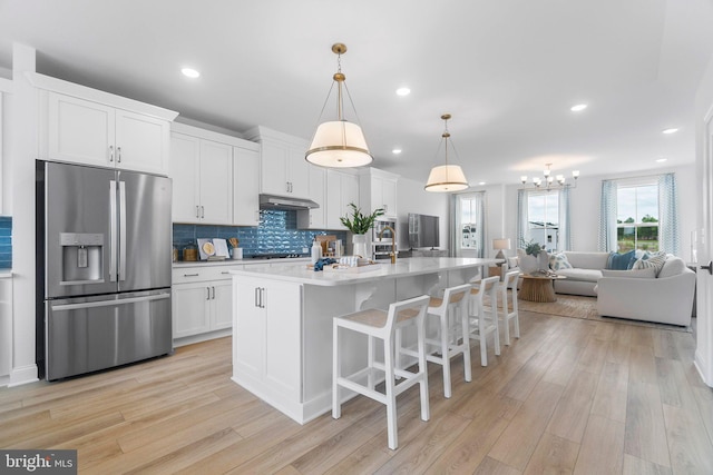 kitchen with stainless steel refrigerator with ice dispenser, a center island with sink, white cabinetry, and light hardwood / wood-style floors