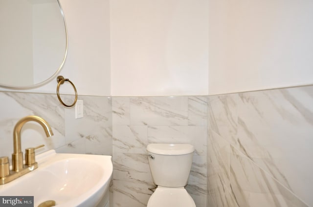 bathroom with toilet, sink, and tile walls