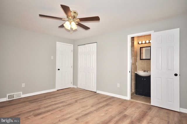 unfurnished bedroom with light hardwood / wood-style floors, ensuite bath, ceiling fan, and tile walls