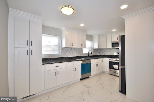 kitchen featuring appliances with stainless steel finishes, backsplash, sink, dark stone countertops, and white cabinets