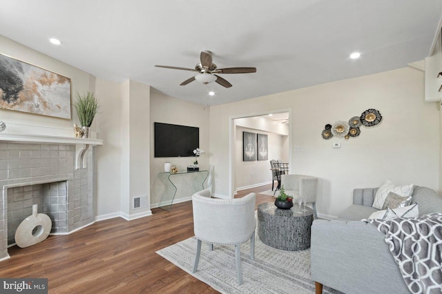 living room featuring ceiling fan, dark hardwood / wood-style flooring, and a brick fireplace