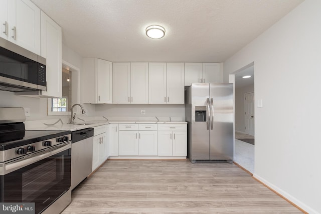 kitchen featuring a textured ceiling, light wood-type flooring, stainless steel appliances, and white cabinetry