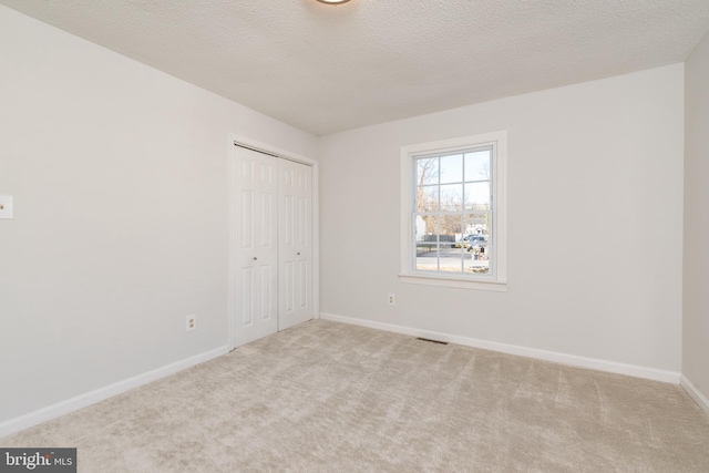 unfurnished bedroom featuring a textured ceiling, light colored carpet, and a closet