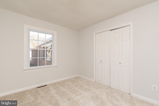 unfurnished bedroom featuring a closet, light colored carpet, and a textured ceiling