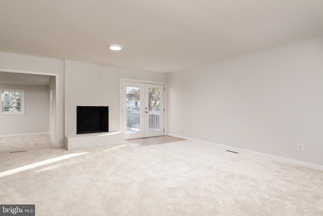 unfurnished living room featuring french doors, carpet floors, a brick fireplace, and a wealth of natural light