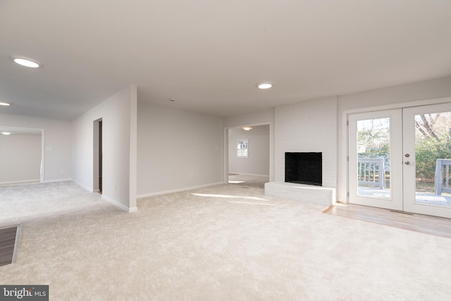 unfurnished living room with light colored carpet, a fireplace, and french doors