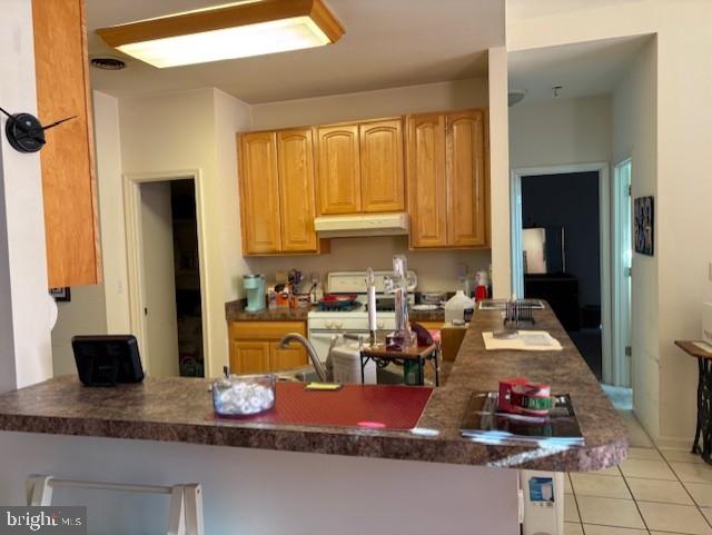 kitchen with white gas range, kitchen peninsula, and light tile patterned floors