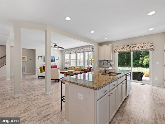 kitchen featuring a kitchen island with sink, sink, ceiling fan, light hardwood / wood-style floors, and light stone counters