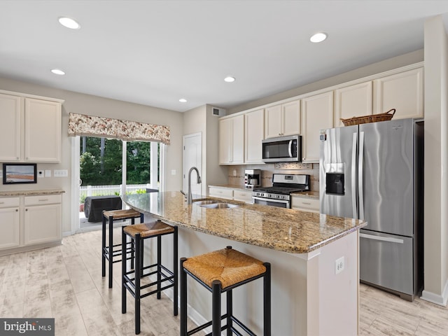 kitchen featuring appliances with stainless steel finishes, light stone counters, a breakfast bar, sink, and an island with sink