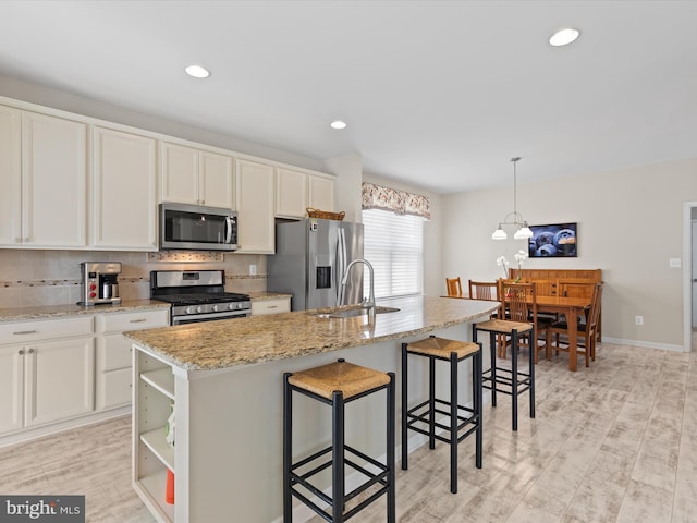 kitchen with sink, light wood-type flooring, an island with sink, appliances with stainless steel finishes, and decorative light fixtures