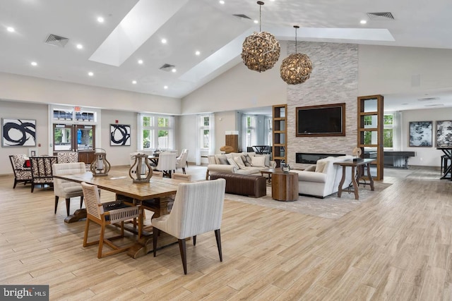 dining area with a fireplace, light hardwood / wood-style floors, high vaulted ceiling, and a skylight