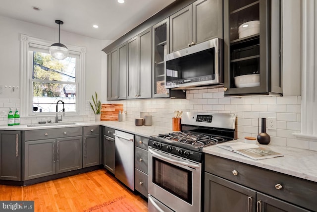 kitchen with sink, hanging light fixtures, stainless steel appliances, decorative backsplash, and light wood-type flooring