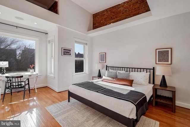 bedroom featuring multiple windows, light hardwood / wood-style floors, and a high ceiling