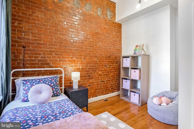 bedroom featuring light wood-type flooring and brick wall