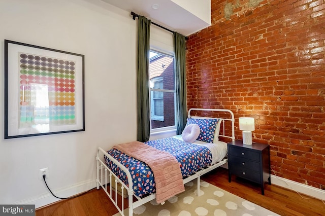 bedroom featuring dark hardwood / wood-style floors and brick wall