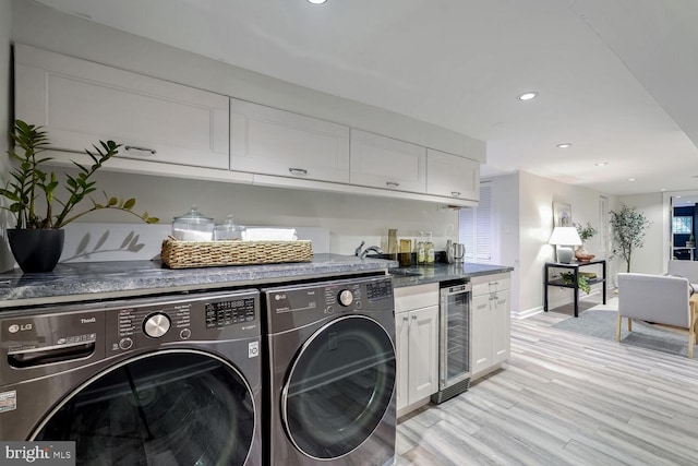 laundry room with washing machine and clothes dryer, wine cooler, sink, and light wood-type flooring