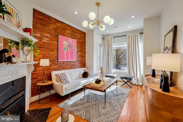 living room featuring hardwood / wood-style flooring, a notable chandelier, crown molding, and brick wall