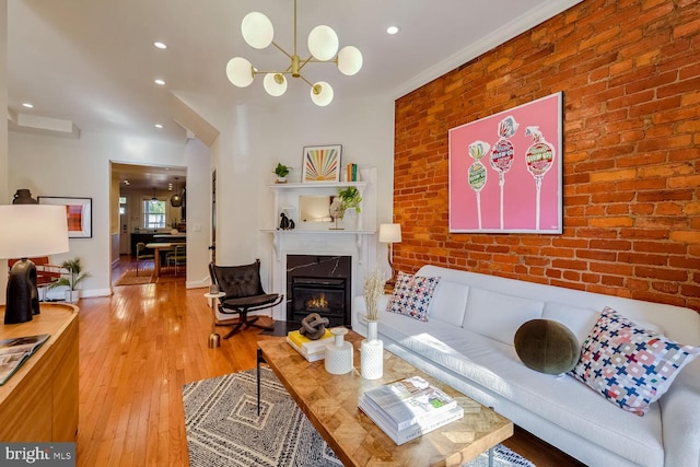 living room featuring a high end fireplace, light hardwood / wood-style floors, brick wall, and a notable chandelier