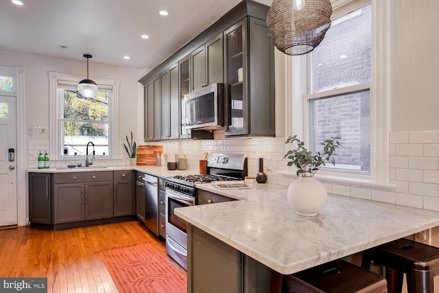 kitchen featuring kitchen peninsula, stainless steel appliances, sink, pendant lighting, and light hardwood / wood-style flooring