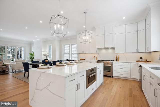 kitchen featuring white cabinets, light hardwood / wood-style flooring, hanging light fixtures, a kitchen island, and appliances with stainless steel finishes