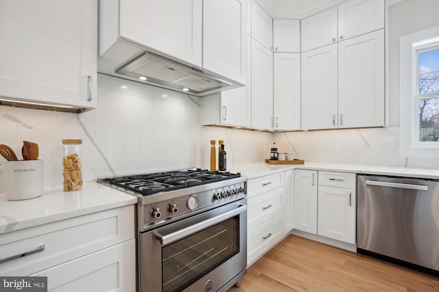 kitchen with exhaust hood, light hardwood / wood-style floors, backsplash, white cabinetry, and appliances with stainless steel finishes