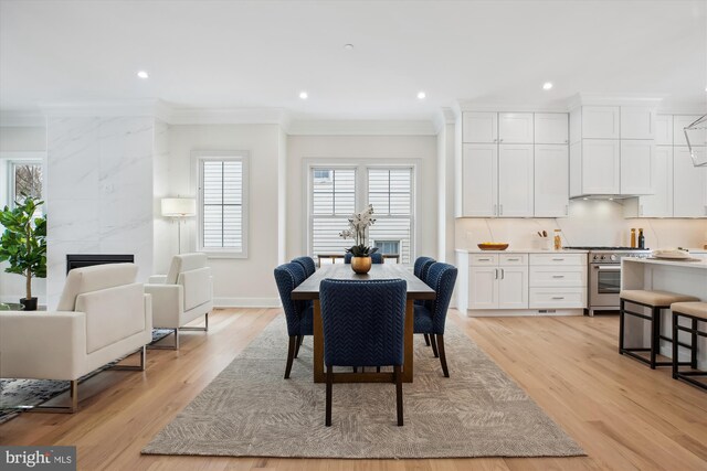 dining space featuring a premium fireplace, ornamental molding, and light hardwood / wood-style flooring