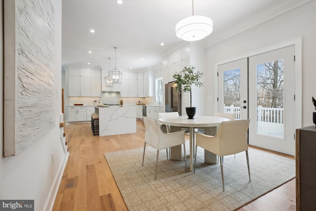 dining area with a healthy amount of sunlight, french doors, ornamental molding, and light wood-type flooring